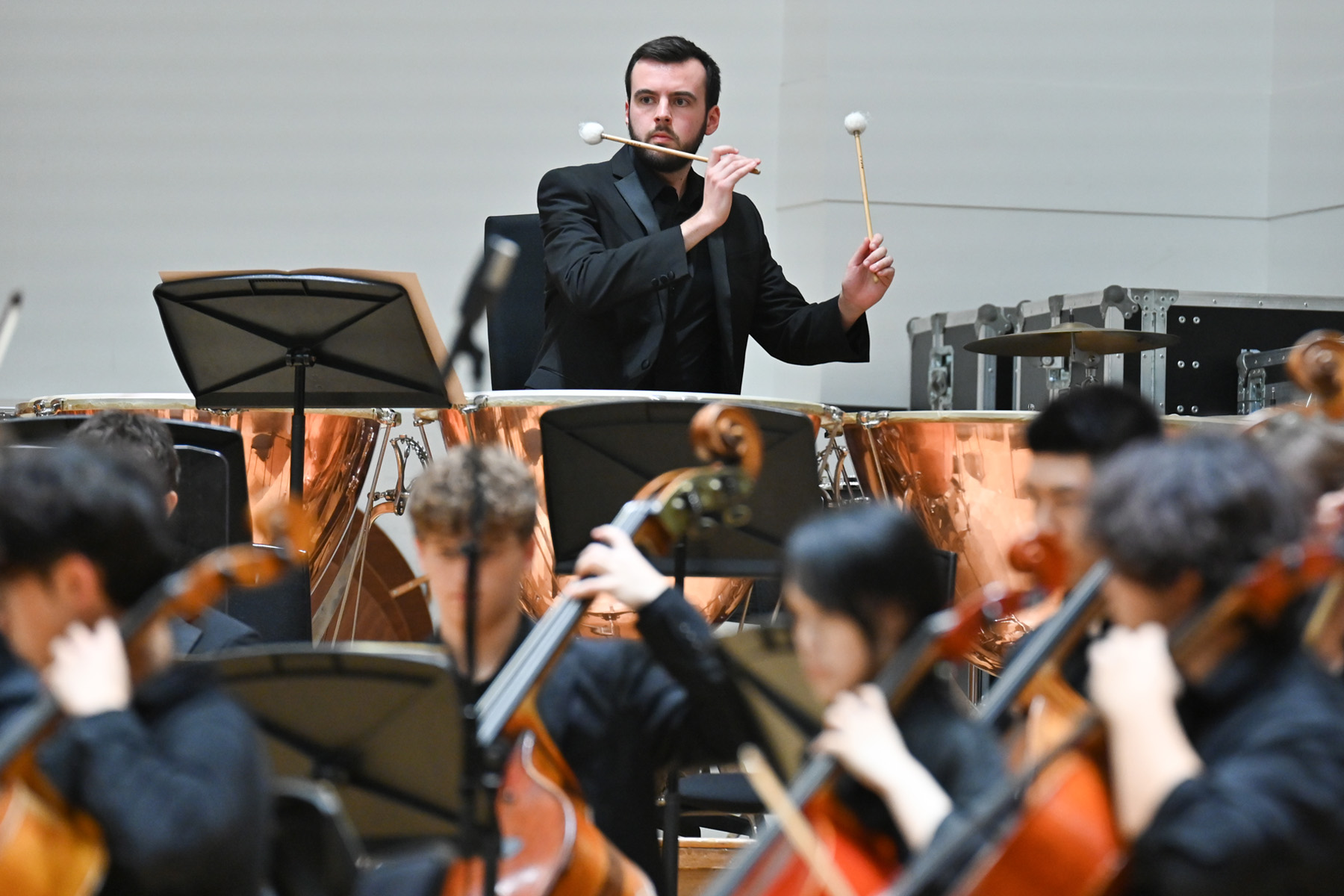 A male student playing the timpani in an orchestral performance.
